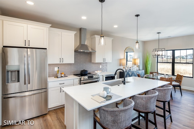 kitchen featuring sink, a center island with sink, stainless steel appliances, and wall chimney exhaust hood