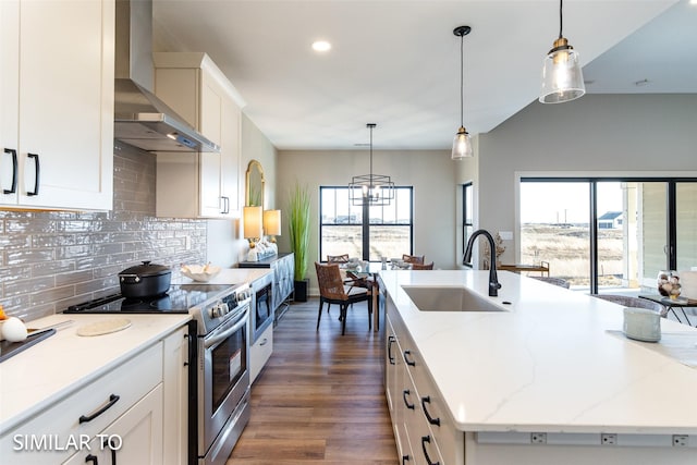 kitchen featuring electric stove, wall chimney range hood, white cabinets, and a kitchen island with sink