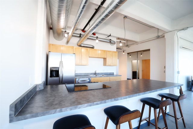 kitchen featuring pendant lighting, a kitchen bar, light brown cabinetry, sink, and stainless steel fridge