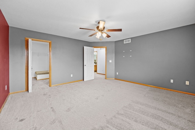 unfurnished bedroom featuring a spacious closet, a closet, light carpet, and ceiling fan