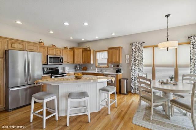 kitchen featuring appliances with stainless steel finishes, hanging light fixtures, a kitchen island, light hardwood / wood-style flooring, and sink