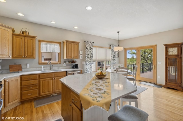 kitchen with a center island, stainless steel dishwasher, sink, light hardwood / wood-style flooring, and hanging light fixtures