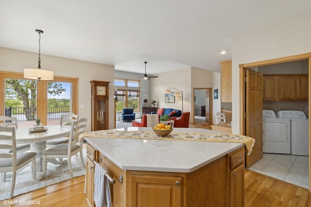 kitchen featuring a kitchen island, washing machine and clothes dryer, hanging light fixtures, light wood-type flooring, and ceiling fan