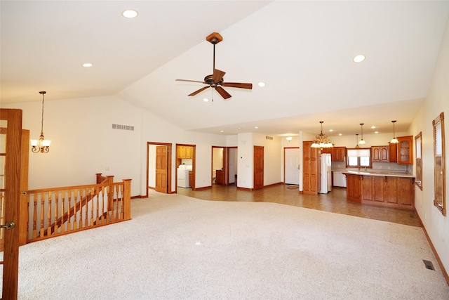 unfurnished living room with high vaulted ceiling, washer / clothes dryer, ceiling fan with notable chandelier, and dark carpet