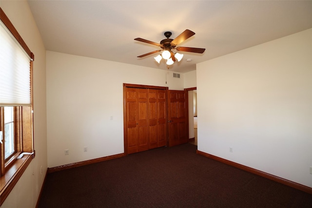 unfurnished bedroom featuring ceiling fan, dark carpet, and a closet