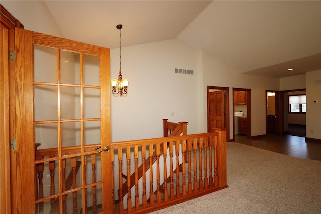 corridor with lofted ceiling, a notable chandelier, and dark colored carpet