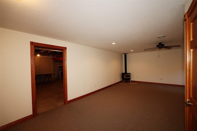 carpeted spare room featuring ceiling fan, a wood stove, and a textured ceiling