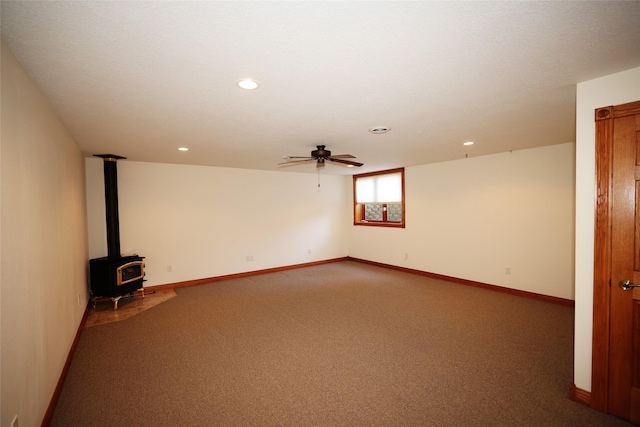 empty room featuring ceiling fan, a wood stove, and carpet