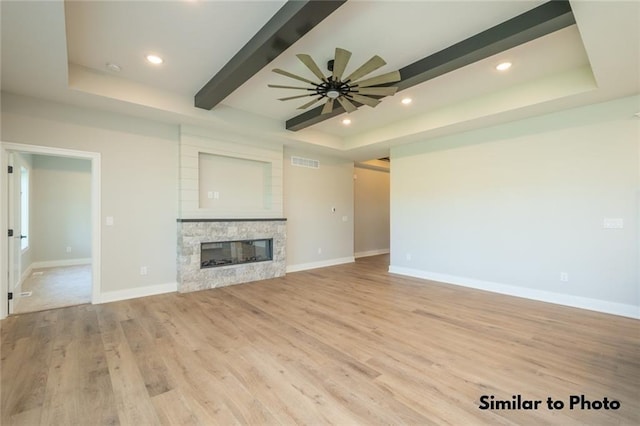 unfurnished living room featuring ceiling fan, light wood-type flooring, a stone fireplace, and a raised ceiling