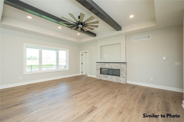 unfurnished living room with ceiling fan, a tray ceiling, a stone fireplace, and light hardwood / wood-style flooring