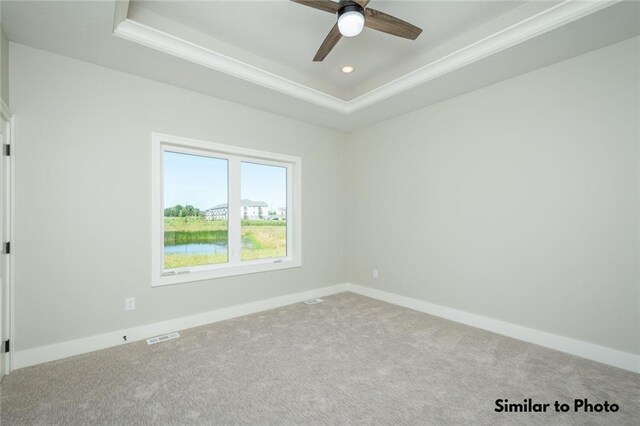 empty room featuring a raised ceiling, ceiling fan, carpet, and ornamental molding