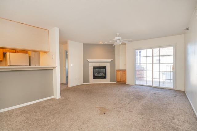 unfurnished living room with light carpet, ceiling fan, and a tile fireplace