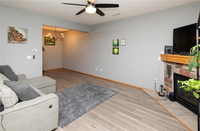 living room with wood-type flooring, a fireplace, and ceiling fan with notable chandelier