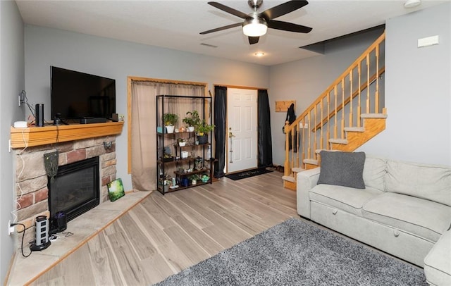 living room featuring ceiling fan, a stone fireplace, and light hardwood / wood-style floors