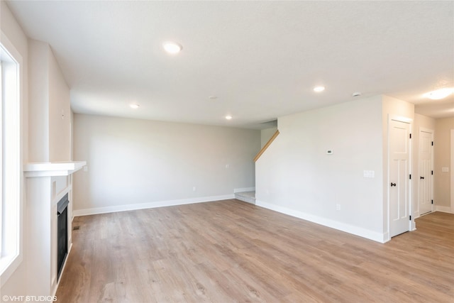 unfurnished living room featuring light wood finished floors, a fireplace, baseboards, and recessed lighting
