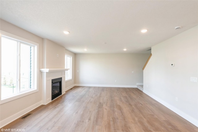 unfurnished living room with recessed lighting, visible vents, light wood-type flooring, baseboards, and a glass covered fireplace