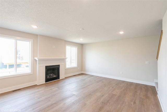 unfurnished living room with recessed lighting, a glass covered fireplace, visible vents, and light wood-type flooring