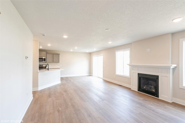 unfurnished living room with recessed lighting, light wood-style floors, a glass covered fireplace, and a sink