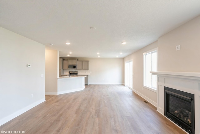 unfurnished living room featuring baseboards, a glass covered fireplace, light wood finished floors, and recessed lighting