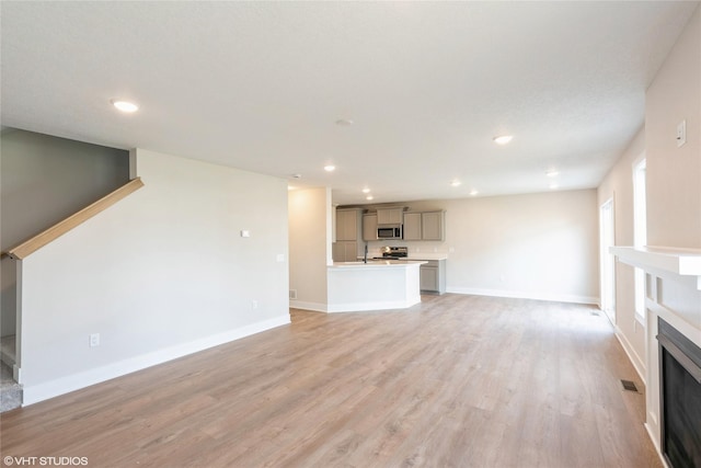 unfurnished living room with light wood finished floors, a fireplace, baseboards, and recessed lighting