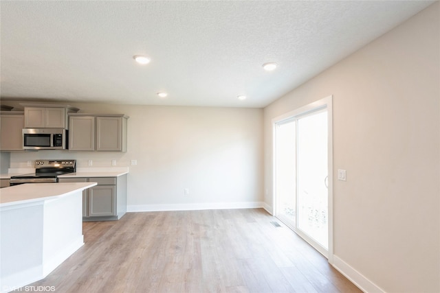 kitchen with stainless steel appliances, light countertops, light wood-type flooring, baseboards, and gray cabinetry