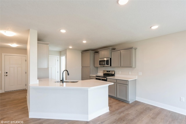kitchen featuring gray cabinetry, a sink, light wood-style floors, and appliances with stainless steel finishes