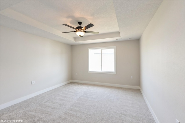 spare room featuring a raised ceiling, a ceiling fan, baseboards, and light carpet