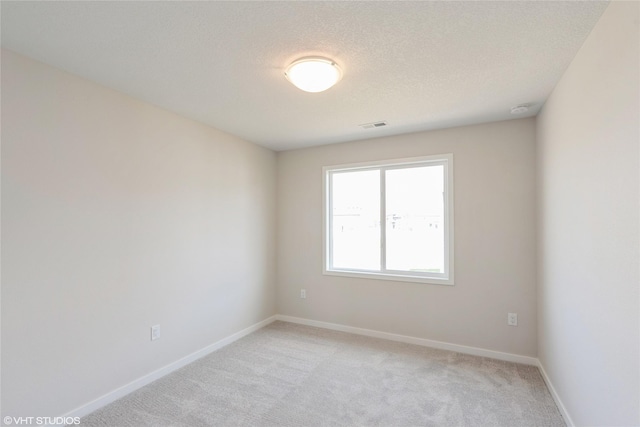 empty room featuring baseboards, visible vents, a textured ceiling, and light colored carpet