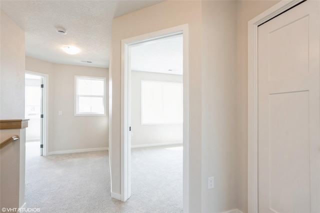 hallway with light carpet, a textured ceiling, and baseboards