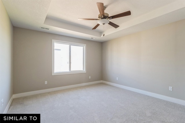 spare room featuring ceiling fan, light carpet, and a raised ceiling