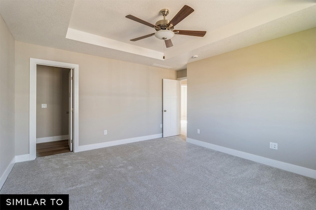 unfurnished bedroom featuring ceiling fan, carpet, and a raised ceiling