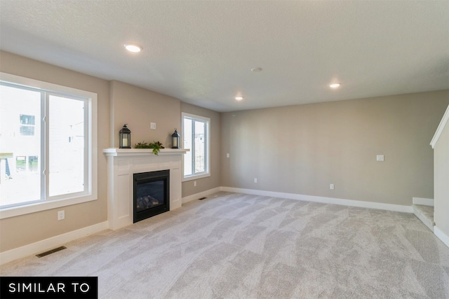 unfurnished living room with a textured ceiling, light carpet, and a healthy amount of sunlight