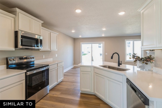 kitchen featuring light hardwood / wood-style flooring, appliances with stainless steel finishes, a textured ceiling, white cabinets, and sink