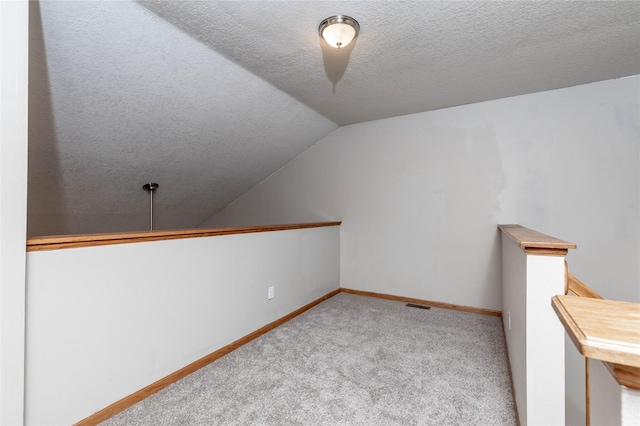 bonus room with lofted ceiling, light colored carpet, and a textured ceiling