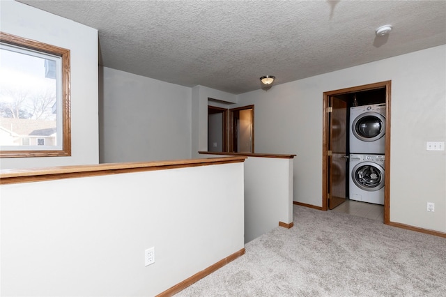 hallway with stacked washer / drying machine, light colored carpet, and a textured ceiling