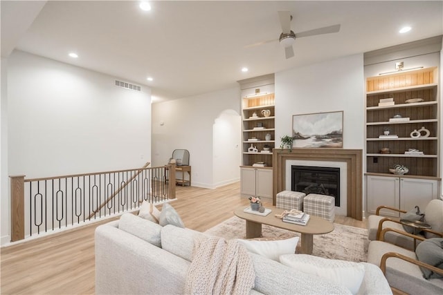 living room featuring ceiling fan, light hardwood / wood-style flooring, and built in shelves