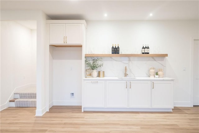 bar with white cabinets, sink, and light hardwood / wood-style flooring