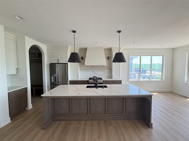 3034 NW Beechwood Dr, Grimes, IA 50111 - kitchen featuring stainless steel fridge, premium range hood, light wood-style flooring, arched walkways, and a textured ceiling