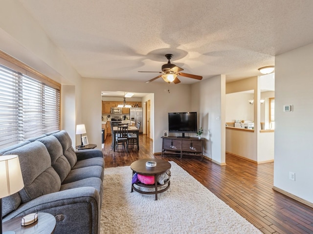 living room with dark hardwood / wood-style flooring, ceiling fan with notable chandelier, and a textured ceiling