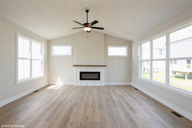 unfurnished living room with a glass covered fireplace, visible vents, light wood-style floors, lofted ceiling, and a ceiling fan