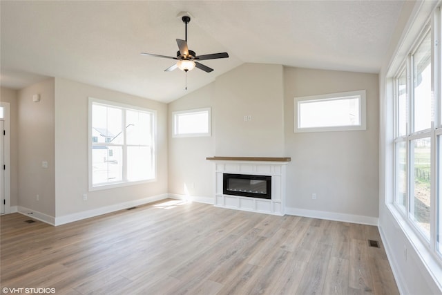 unfurnished living room featuring lofted ceiling, light wood finished floors, visible vents, a ceiling fan, and a glass covered fireplace
