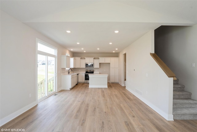 unfurnished living room with stairs, a sink, light wood-style floors, visible vents, and recessed lighting