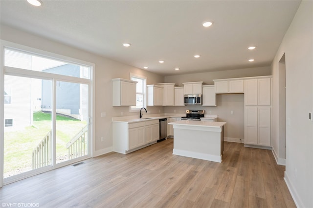 kitchen with a sink, light wood-style floors, stainless steel appliances, baseboards, and a kitchen island