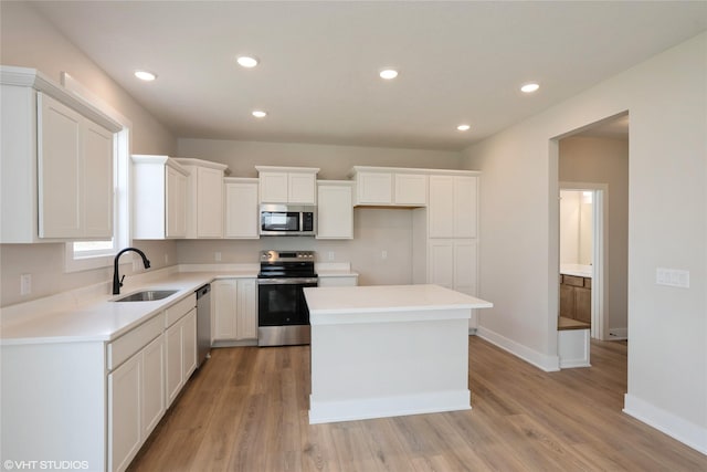 kitchen with white cabinets, light wood finished floors, stainless steel appliances, and a sink