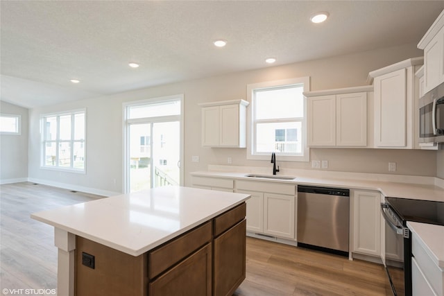 kitchen featuring light wood finished floors, white cabinets, a sink, a kitchen island, and appliances with stainless steel finishes
