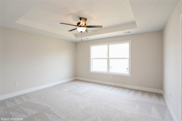 spare room with ceiling fan, light carpet, a tray ceiling, baseboards, and visible vents