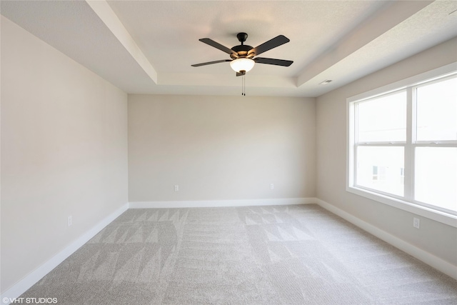 empty room with light carpet, a ceiling fan, a tray ceiling, and baseboards