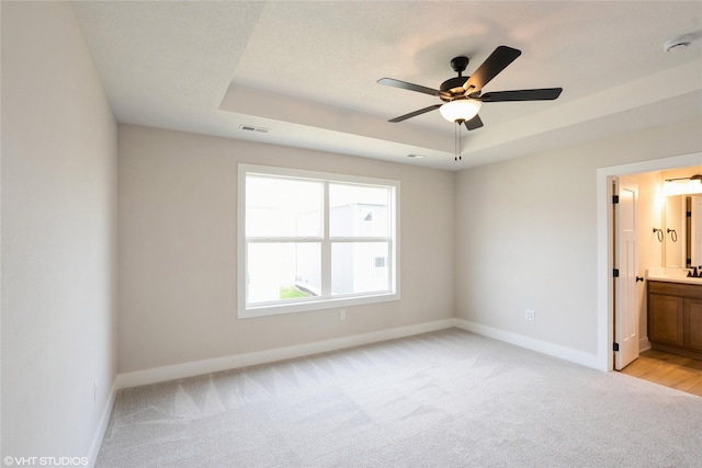 unfurnished bedroom featuring baseboards, visible vents, a raised ceiling, and light colored carpet