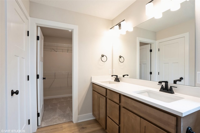 full bath featuring a walk in closet, wood finished floors, a sink, and double vanity