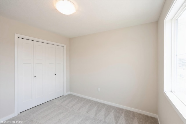 unfurnished bedroom with baseboards, a closet, and light colored carpet